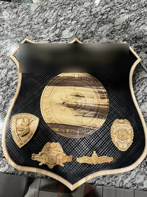 Command farewell shield: Carved medallion, badges and warfare insignia on a diamond-cut black field with a maple edge.